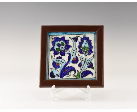 20th century AD. A square glazed ceramic tile featuring flowers and foliage within a blue border; mounted in a wooden frame. 