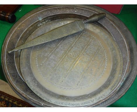 A collection of four Indian engraved brass trays, an Indian brass sheathed and handled dagger, an Indian foliate carved ebony