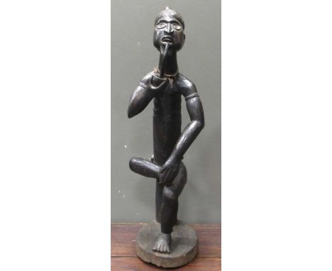 A 20th century African carved figure of seated male smoking a pipe, mirror insert to the side of the torso 101cm high
