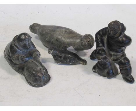 A collection of four soapstone Inuit carvings, including two seals and two hunters. Markings on the bases of each figure visi
