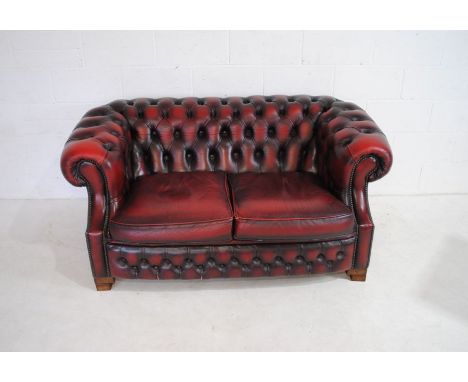 A two seater oxblood leather Chesterfield sofa with button-back detailing