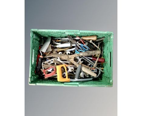 A crate containing a quantity of vintage hand tools including spanners, hand saws, garden tools.