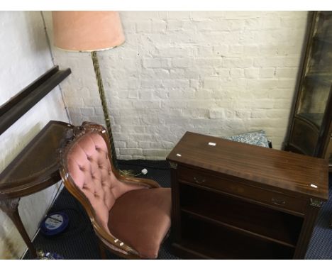 A small mahogany book shelf, mahogany nursing chair with pink upholstery, a mahogany desk and brass floor lamp.