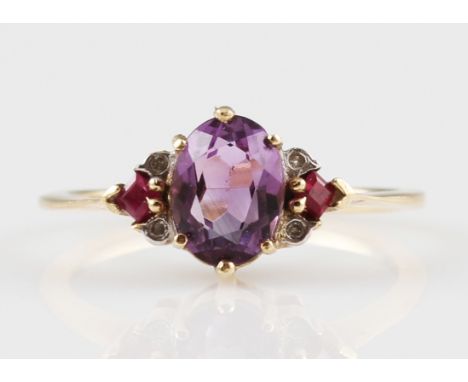 A 9ct yellow gold amethyst and ruby ring, set with a central oval cut amethyst, approx. 8x6mm, flanked to either side with a 