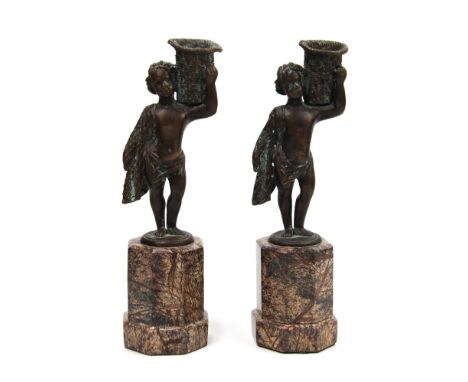 A pair of candelabra, with boys wrapped in togas,  bearing baskets atop their shoulders, standing on  marble bases with brown