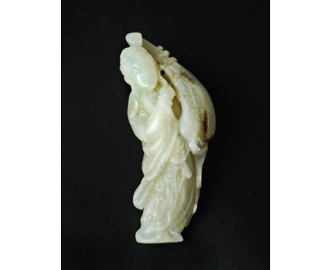 A jade toggle light green in color with a few dark  inclusions carved into a bowed figure of a female  musician holding a pip