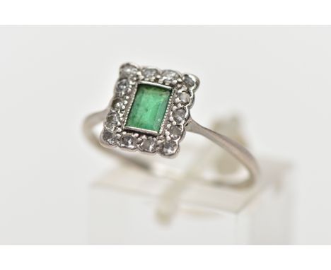 A WHITE METAL EMERALD AND DIAMOND RING, of a rectangular form, centring on a rectangular cut emerald, milgrain set within a s