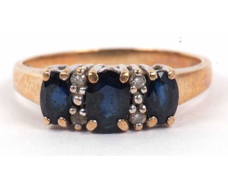 A sapphire and diamond three stone ring featuring three oval faceted graduated sapphires, highlighted between with four small