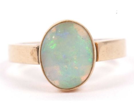 A single stone opal ring, cabochon cut and set in a cut down milligrain edge setting, 10 x 8 mm approx, stamped 10k, size L/M