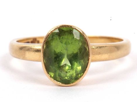 An 18ct gold and peridot ring, the oval cut faceted peridot in rub over setting to a plain polished shank stamped with a Mill