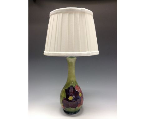 A Moorcroft Clematis pattern table lamp, tube lined with large flowerheads, in tones of purple and red on a mottled green gro