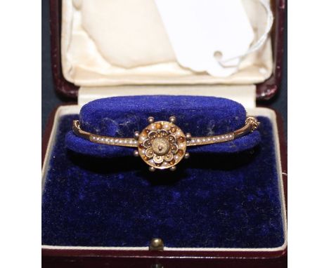 A precious yellow metal hinged bangle, the front with filigree work floral mount bordered by capstan wheel set alternating se