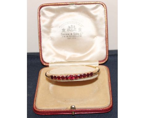 An 18ct yellow gold and red stone hinged bangle, claw set eleven graduated red stones with pierced gallery to sides, stamped 