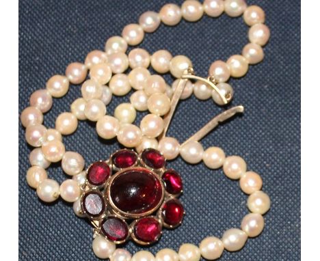 A triple row cultured pearl bracelet, having large precious yellow metal clasp, set oval cabochon garnet to centre surrounded