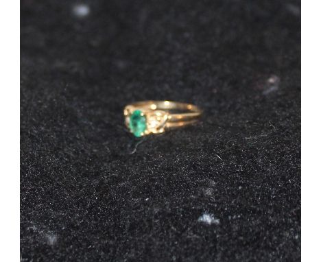 A 9ct. yellow gold, emerald and diamond ring, claw set oval cut emerald to centre and single round cut diamond to each should