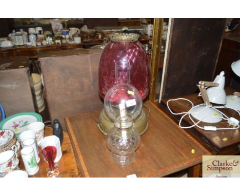 A brass Edwardian heater with cranberry glass shade together with one other glass oil lamp