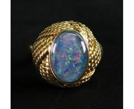 A gold ring mounted with an oval opal doublet, within a cast ropetwist surround, detailed indistinctly 18 CT, ring size O 1/2