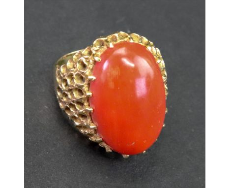 A gold and coral dress ring, the large oval polished coral of orange red colour, claw set, with pierced and textured shoulder