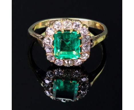 A gold, emerald and diamond cluster ring, mounted with the square step cut emerald at the centre, in a surround of smaller cu