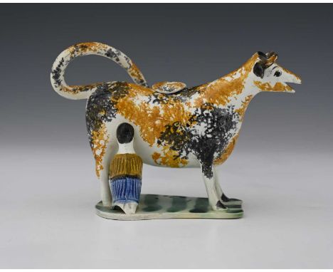 An early 19th Century Prattware cow creamer and cover, milkmaid and pail beneath, the cow with ochre and black sponged decora