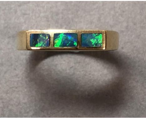 A three stone black opal ring set in 18ct gold, the narrow linear front of the ring rubover set with three rectangular black 