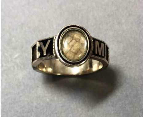 A memorial enamel and hairwork ring, the centre set with an oval glazed panel containing plaited blonde hair, in a black enam