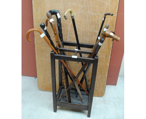 An oak four section stick stand with drip tray containing a collection of walking sticks including a horn handled example wit