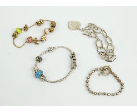 Four fashion bracelets comprising Gucci ball link example with T-bar, a silver gilt JAA charm bracelet, a similar example sta