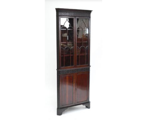 A mahogany corner cupboard with fretwork dentil cornice, two glazed arch sectioned doors opening to three shelves over two pa