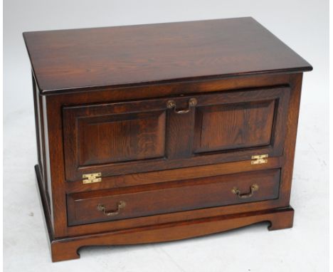A reproduction oak television stand with horizontal hinged cupboard door above single drawer with shaped apron on bracket fee
