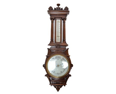 A large early 20th century carved oak aneroid barometer, the thermometer flanked by fluted pillars within and ornately carved