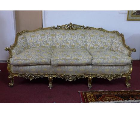 A three seater giltwood settee, with elaborate c-scroll and floral carved giltwood frame, on c-scroll feet, with Art Nouveau 