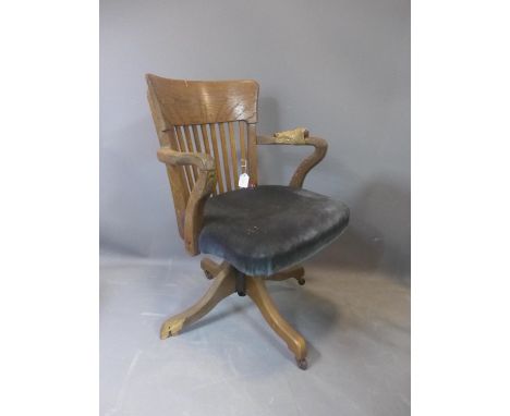 An early 20th century oak swivel desk chair, raised on ceramic castors, (one foot broken - needs restoration), H.84cm 