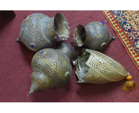 Four Middle Eastern light shades, to include three brass examples with pierced floral decoration and multi-coloured glass ape