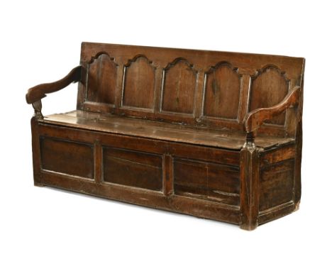 A Georgian oak box settle, the five panel back over a hinged seat enclosing a box interior, the seat flanked at either end by