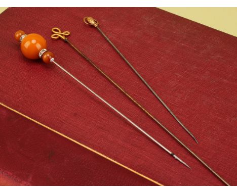 An Art Nouveau 9ct gold hat pin, 16.5cm long, Charles Horner, Chester; an amber three-ball hat pin, 18.5cm long; a 9ct gold t
