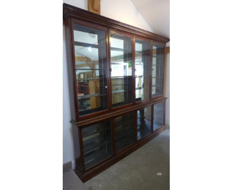 A late Victorian/Edwardian shop display cabinet with a glazed four door top above a glazed four door base both having adjusta