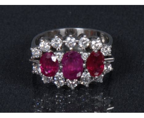 A ruby and diamond ring, three graduated oval pinky red rubies, each divided by a pair of diamond accents, surrounded by a ba