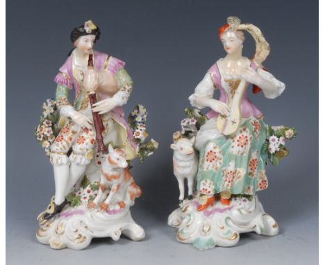 A pair of Derby Patch Mark figures, of a shepherd and shepherdess, he seated wearing feathered headdress, fanciful dress, dog