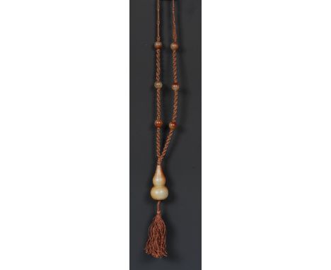 A Chinese russet jade pendant, carved as a double gourd, 4.5cm long, mounted on a woven cord necklace, with six conforming sp
