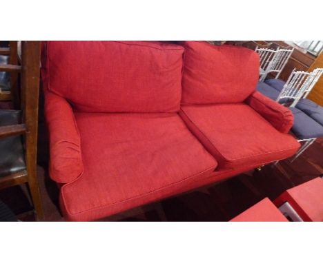 A contemporary two seater sofa with red linen upholstery raised on turned pine legs and castors 