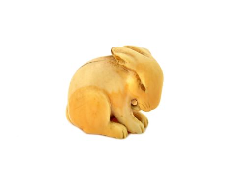 A Japanese ivory netsuke of a hare, 19th century, carved sitting and licking its right foreleg, the eyes inlaid, signed Ranic