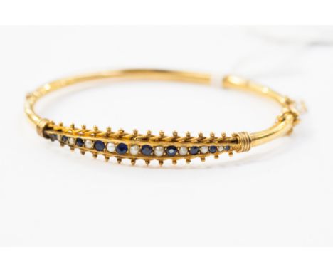 A gold bangle set with sapphires and seed pearls.