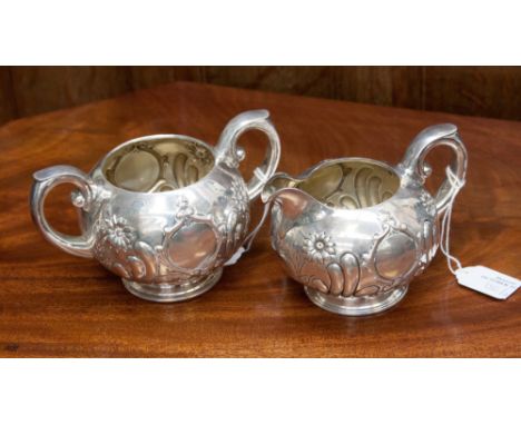 An early twentieth century American sterling silver cream jug and sugar basin with floral embossed decoration on spreading ci