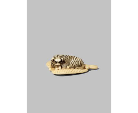 A JAPANESE IVORY NETSUKE MEIJI 1868-1912 Carved as a long-haired Pekingese dog resting on a large palm leaf fan, the eyes inl