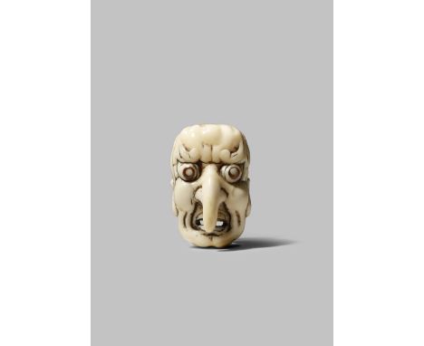 A JAPANESE IVORY NETSUKE MEIJI 1868-1912 Carved as a grimacing tengu mask with a crooked nose, its pupils inlaid with horn, w