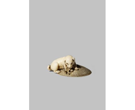 A JAPANESE IVORY NETSUKE MEIJI 1868-1912 Depicting a puppy lying on a large straw hat and gnawing at a section of it, unsigne