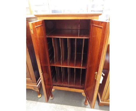 An early 20thC walnut music cabinet, the twin panelled doors enclosing twelve compartments and single shelf, raised on squat 