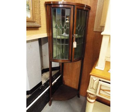 An Edwardian boxwood strung mahogany bow fronted corner cabinet, the lead lit stained glass doors opening to reveal a velvet 