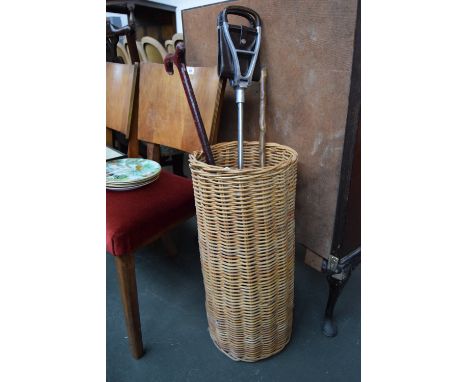 Two walking sticks and a metal shooting stick with leather seat, in a wicker basket